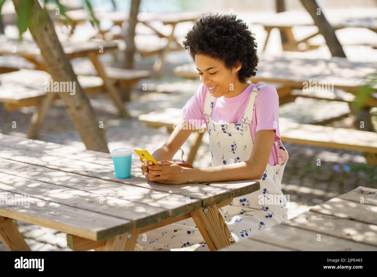 Content black woman surfing cellphone at wooden table Stock Photo