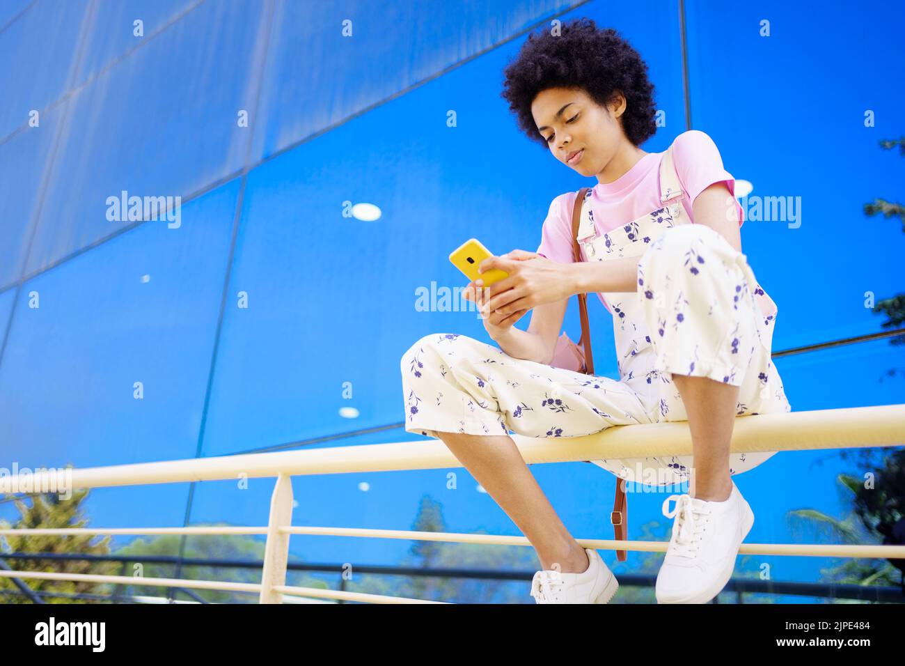 Black woman surfing cellphone on railing Stock Photo