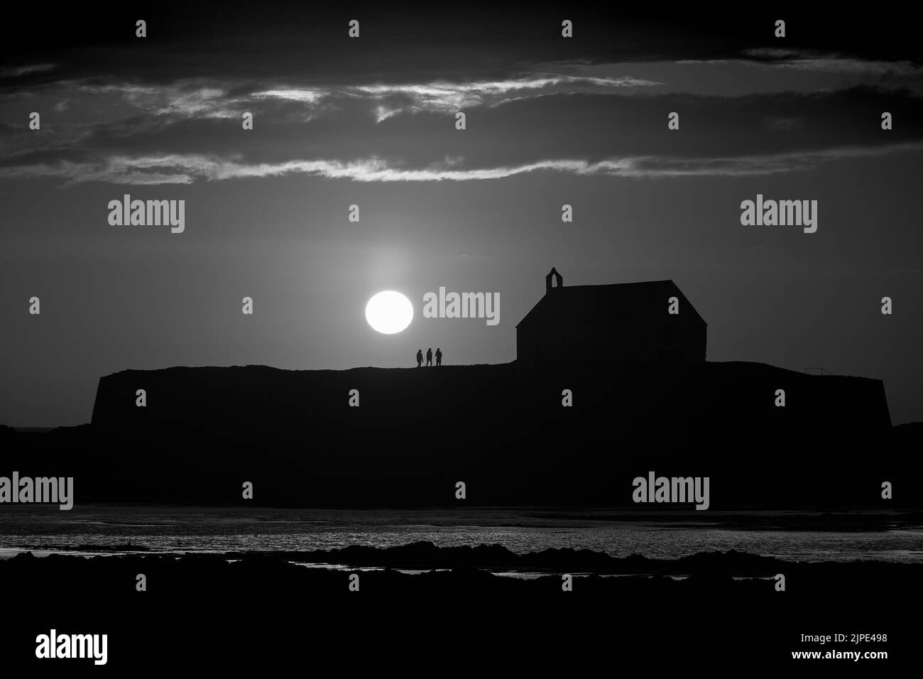 St Cwyfan's Church, known as 'The Church in the Sea' during sunset in Anglesey in North Wales.  Contains unidentifiable silhouettes of people. Stock Photo