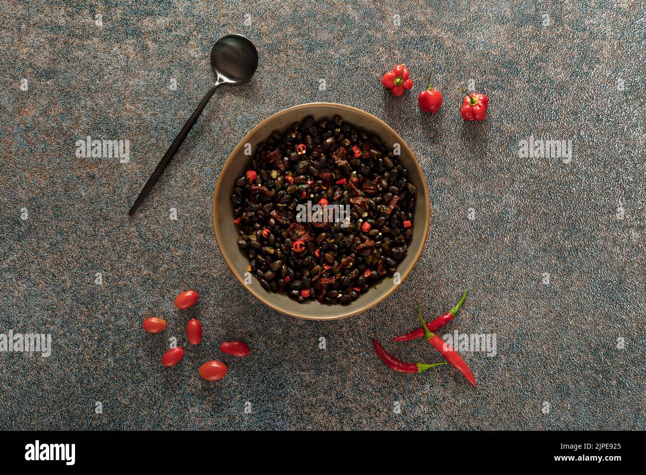 Black beans with dried tomatoes and red Cayenne chili peppers in a brown dish. Stock Photo
