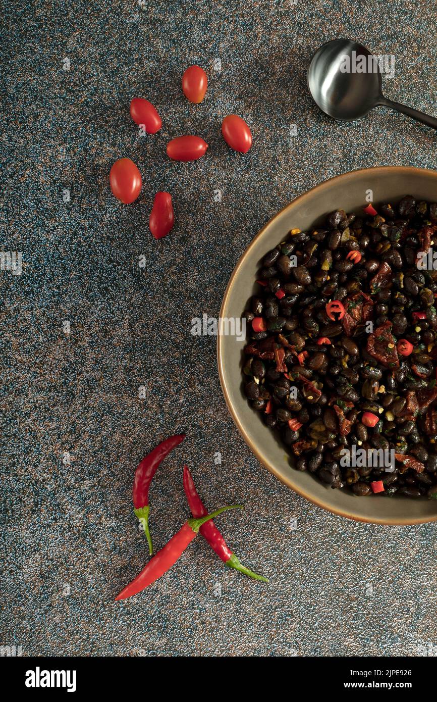 Black beans with dried tomatoes and red Cayenne chili peppers in a brown dish. Stock Photo