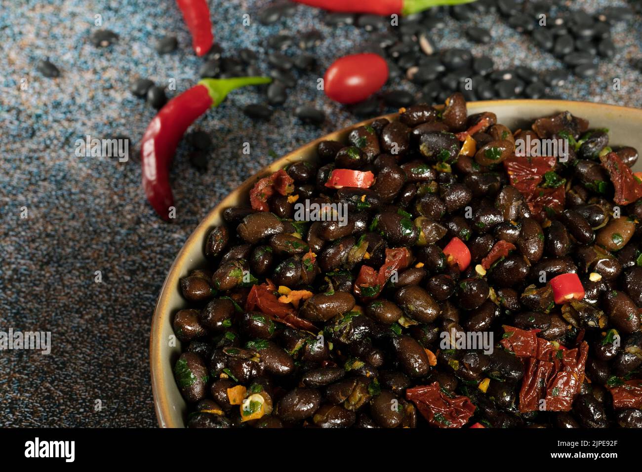 Macro close up of black beans with dried tomatoes and red Cayenne chili peppers in a brown dish. Stock Photo