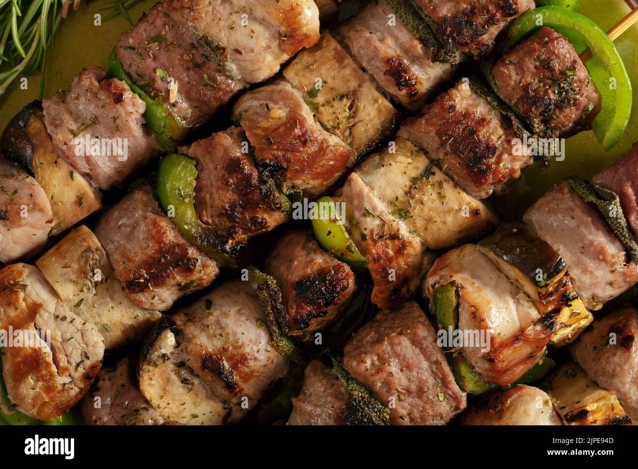 Macro close up of baked meat skewers on a green dish with sage leaves, salt and mixed pepper. Stock Photo