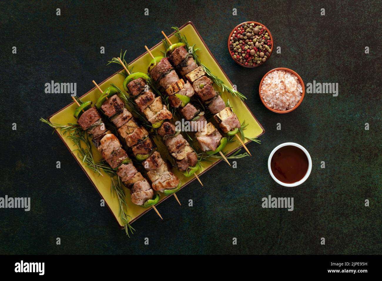 Baked meat skewers on a green dish with salt and mixed pepper. Stock Photo