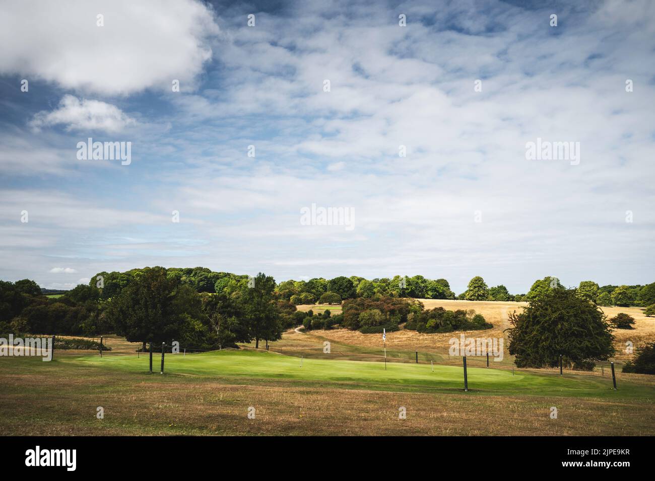 Golf course covered in dry grassland with green grass over hole from watering  during extreme heatwave all under blue sky in summer in Beverley, UK. Stock Photo