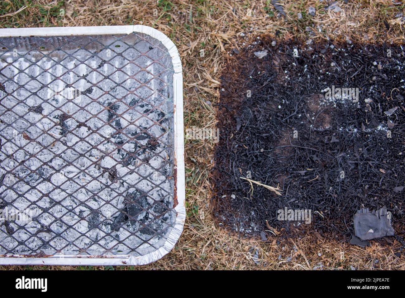 Close up of used disposable barbecue left as rubbish at UK countryside beauty spot - dangerous fire hazard with scorched grass underneath in heatwave! Stock Photo