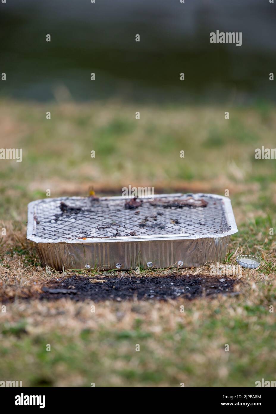 Close up of used disposable barbecue left as rubbish at UK countryside beauty spot - dangerous fire hazard with scorched grass underneath in heatwave! Stock Photo