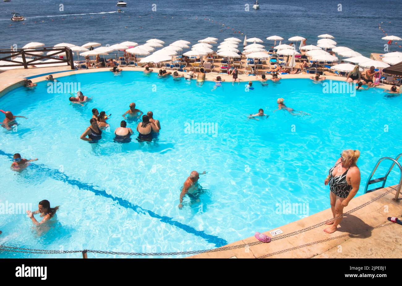 Bugibba, Malta - August 15 2022: High-angle view of a beach resort swimming pool with people bathing and relaxing Stock Photo