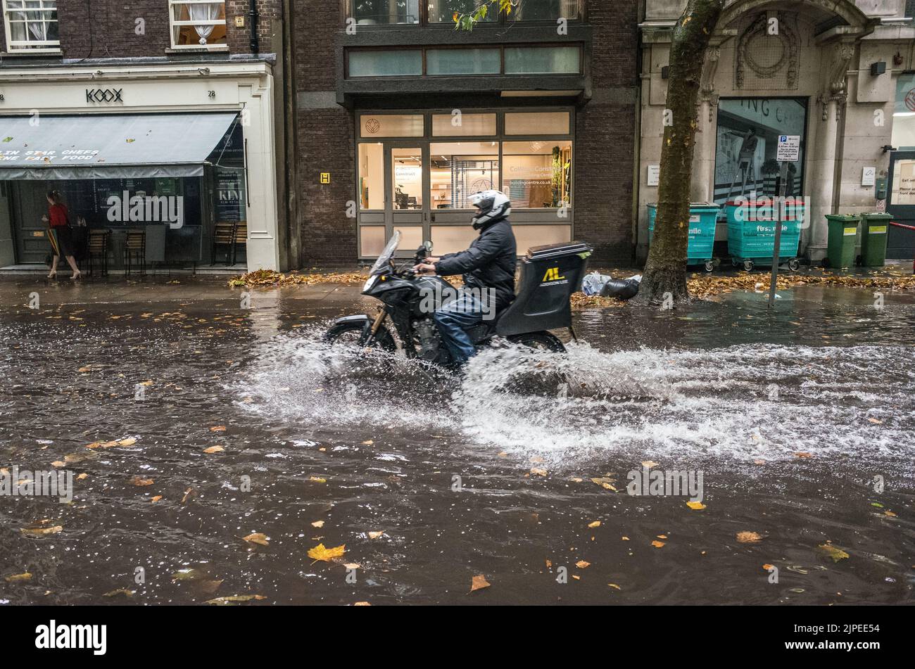 Bike courier rides through flooded road after storm in Central London, England, UK. Stock Photo