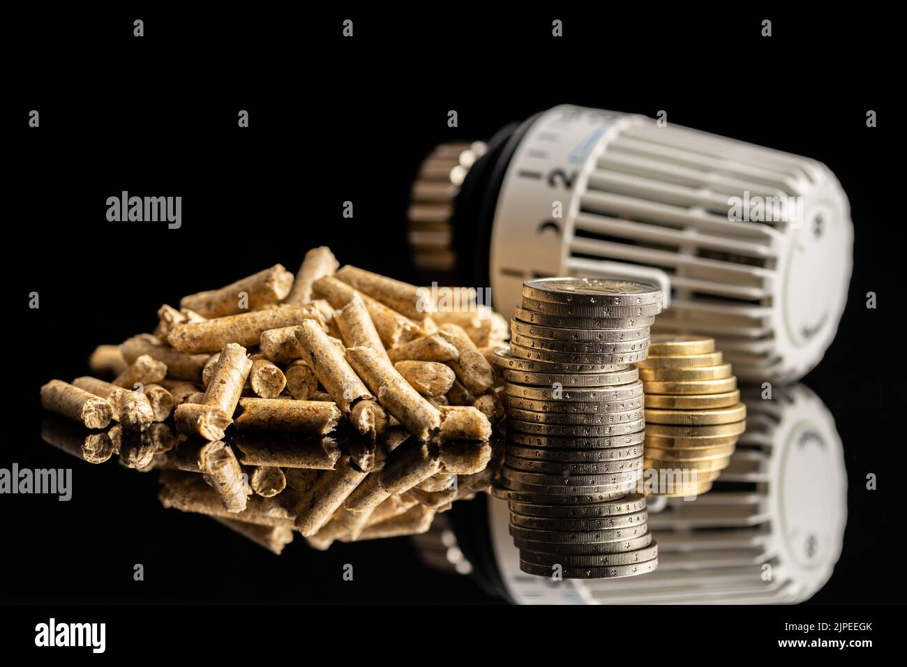 Wooden pellets, coins and thermostatic valve head on black background. Biomass - Renewable source of heating. Stock Photo