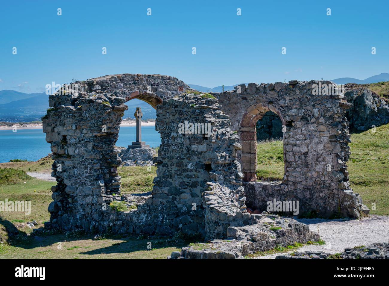 The ruins of St Dwynwens Church on the Island of Anglesey. The celtic cross is seen through the window of the church Stock Photo
