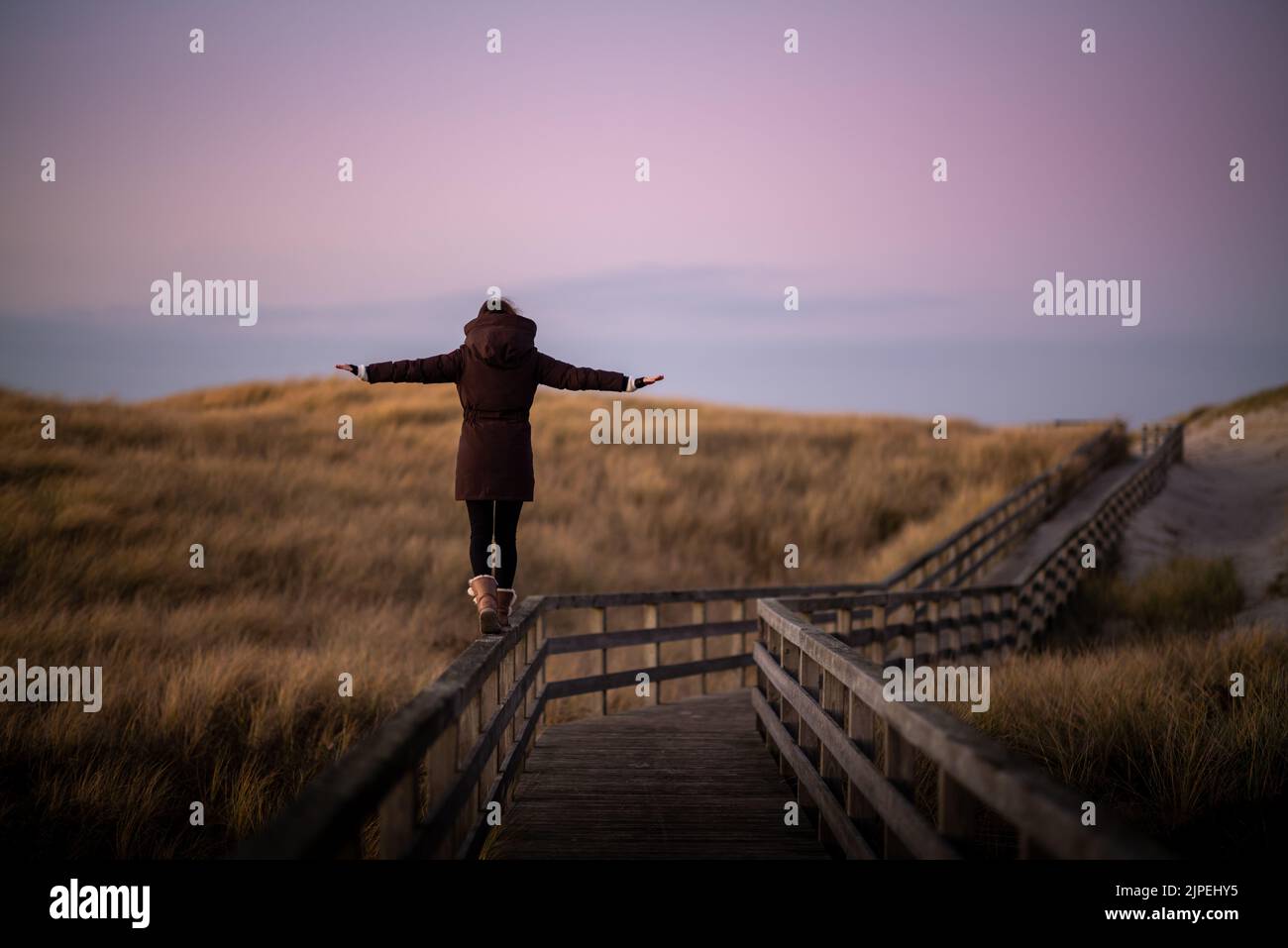 Young woman balances on boardwalk on Sylt, Germany. Stock Photo