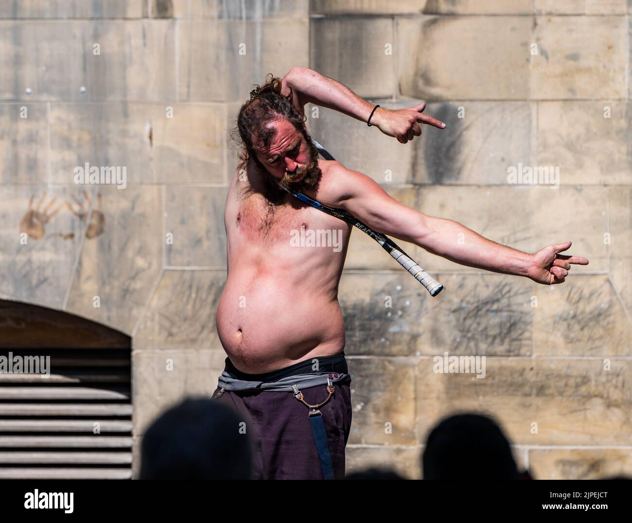 Royal Mile, Edinburgh, Scotland, UK, 17th August 2022. Performers on Royal Mile in the sunshine. Pictured: a street performer contortionist pulls himself through the head of a tennis racquet in front of  a crowd of people. Credit: Sally Anderson/Alamy Live News Stock Photo