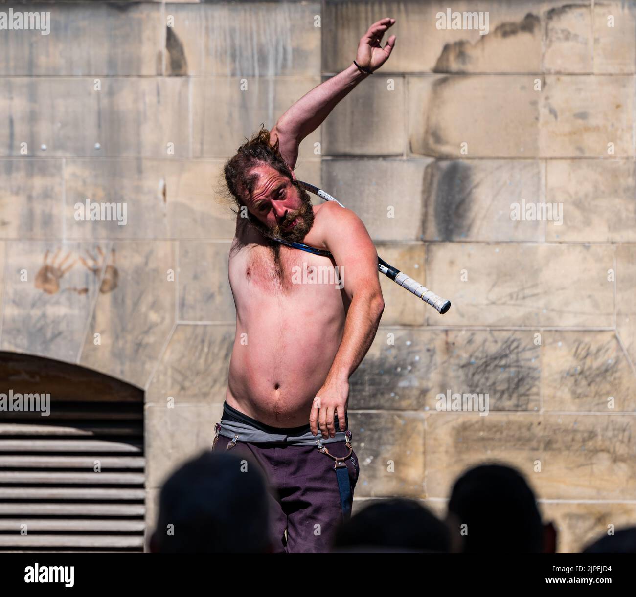 Royal Mile, Edinburgh, Scotland, UK, 17th August 2022. Performers on Royal Mile in the sunshine. Pictured: a street performer contortionist pulls himself through the head of a tennis racquet in front of  a crowd of people. Credit: Sally Anderson/Alamy Live News Stock Photo