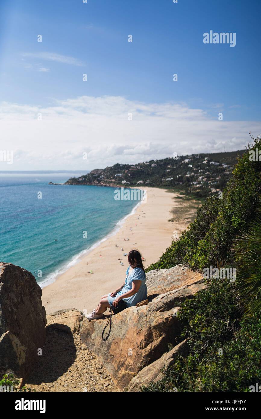 A woman sitting on the cliffs above the sea shore enjoying the view ...