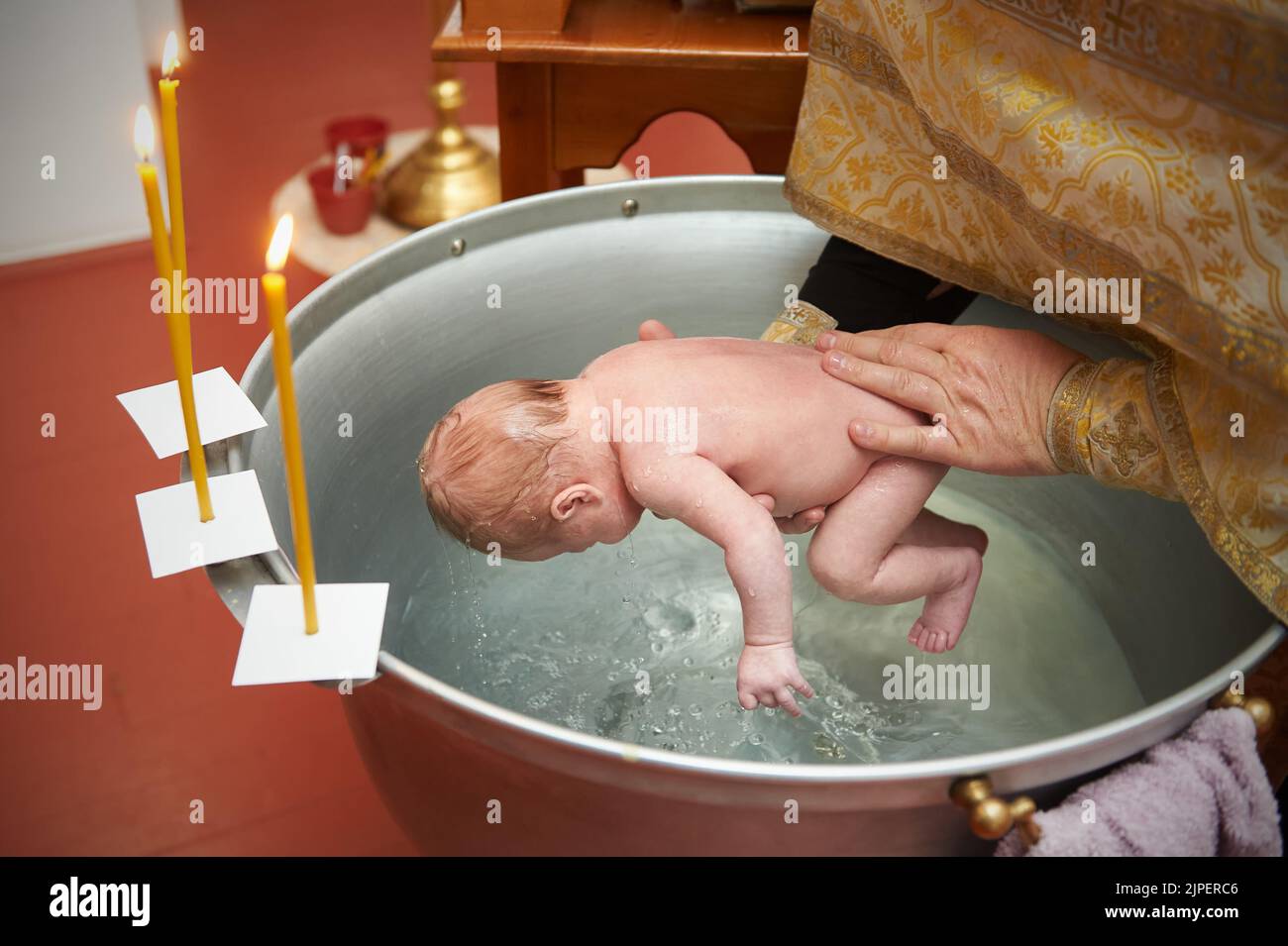 Priest baptizes the newborn by dipping him into the water Stock Photo