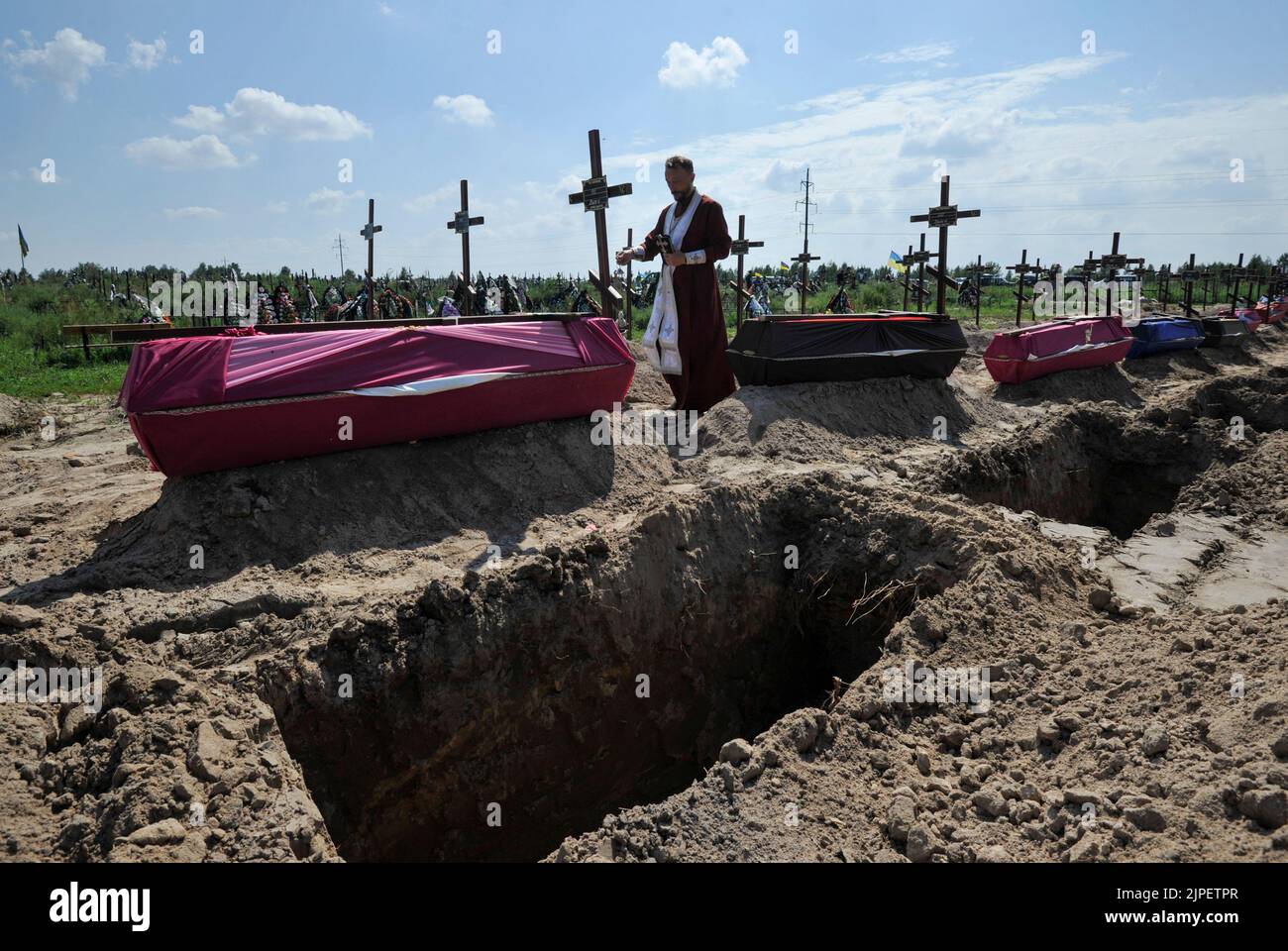An Orthodox priest reads a prayer at the graves of unidentified civilians who were killed by the Russian military during the occupation of the city of Bucha. On Wednesday, 21 unidentified people who were killed by the Russian military in February-March 2022 were buried at the local cemetery. Russia invaded Ukraine on 24 February 2022, triggering the largest military attack in Europe since World War II. Stock Photo