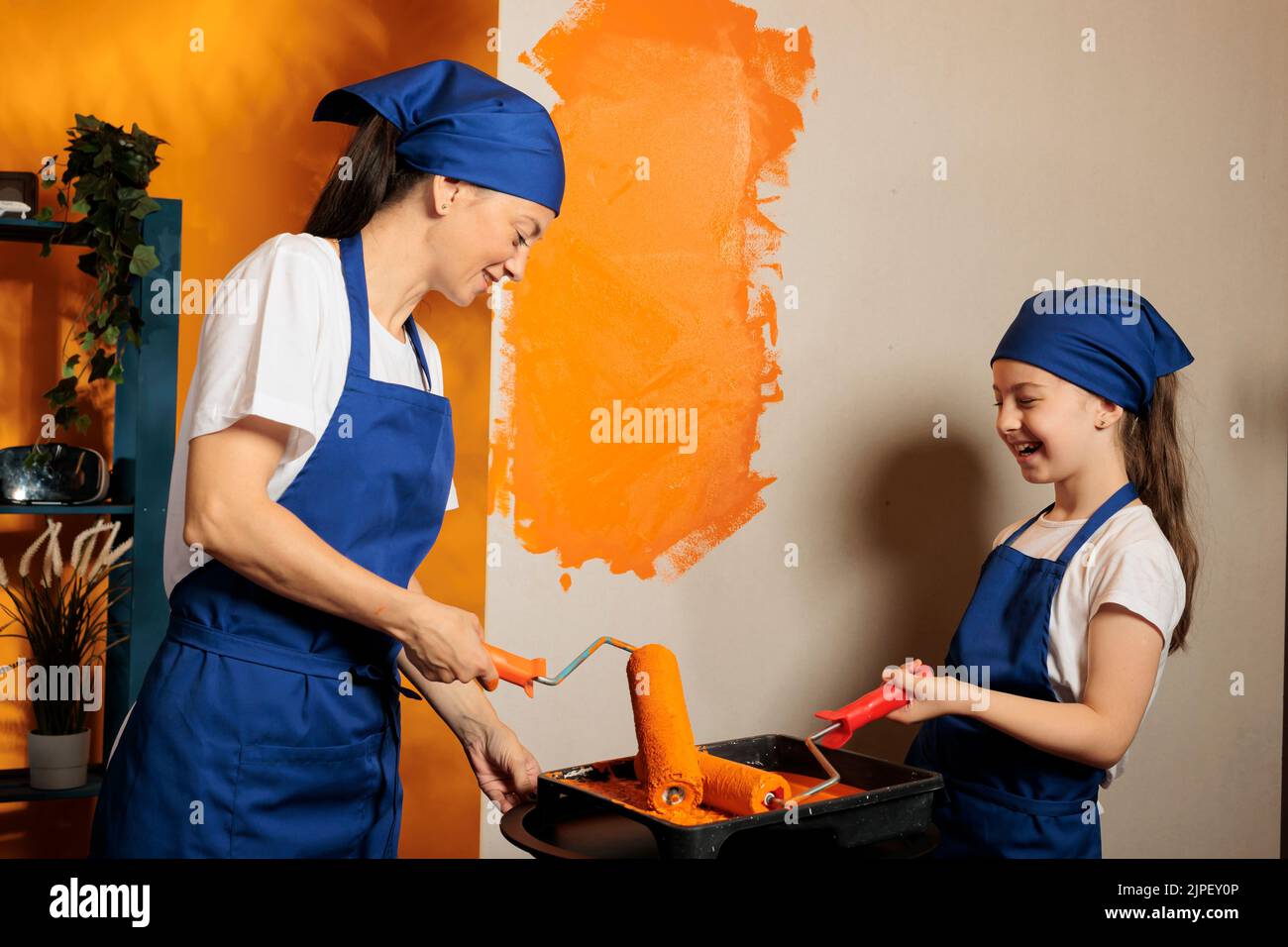 Adult and child using roller brush to paint walls with orange color
