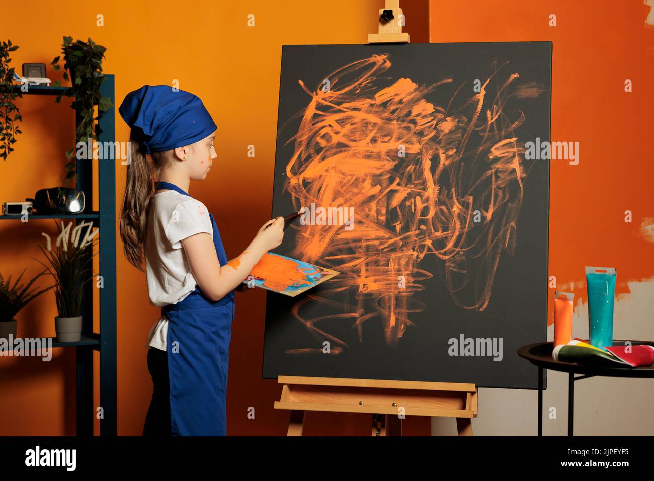 Young child using orange paint color on canvas, creating artwork masterpiece with colormix tray and aquarelle palette. Painting inspiration design with painbrush, watercolor and skills. Stock Photo