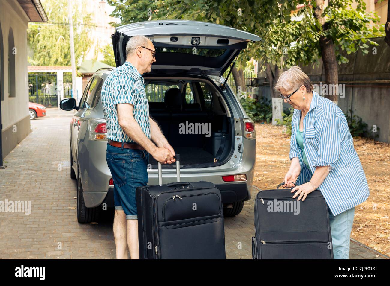 Elderly husband and wife going on holiday vacation and putting luggage or travelling bags in