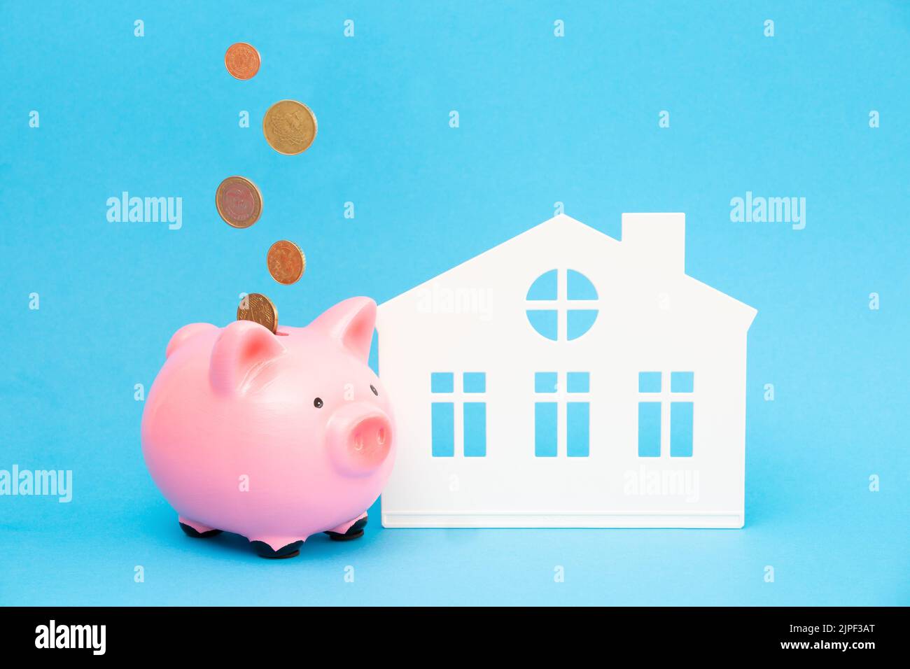 Coins are falling into a pink piggy bank near the house on a blue ...