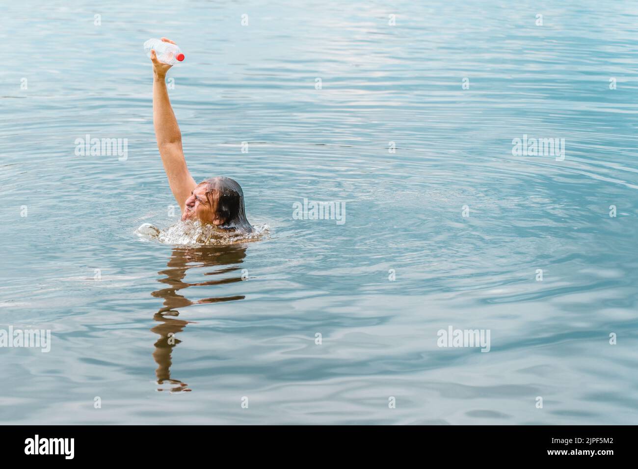 Emerging from water person success man winning moment. Save ocean plastic pollution. Arm raised hand holding bottle plastic garbage beach pollution Stock Photo
