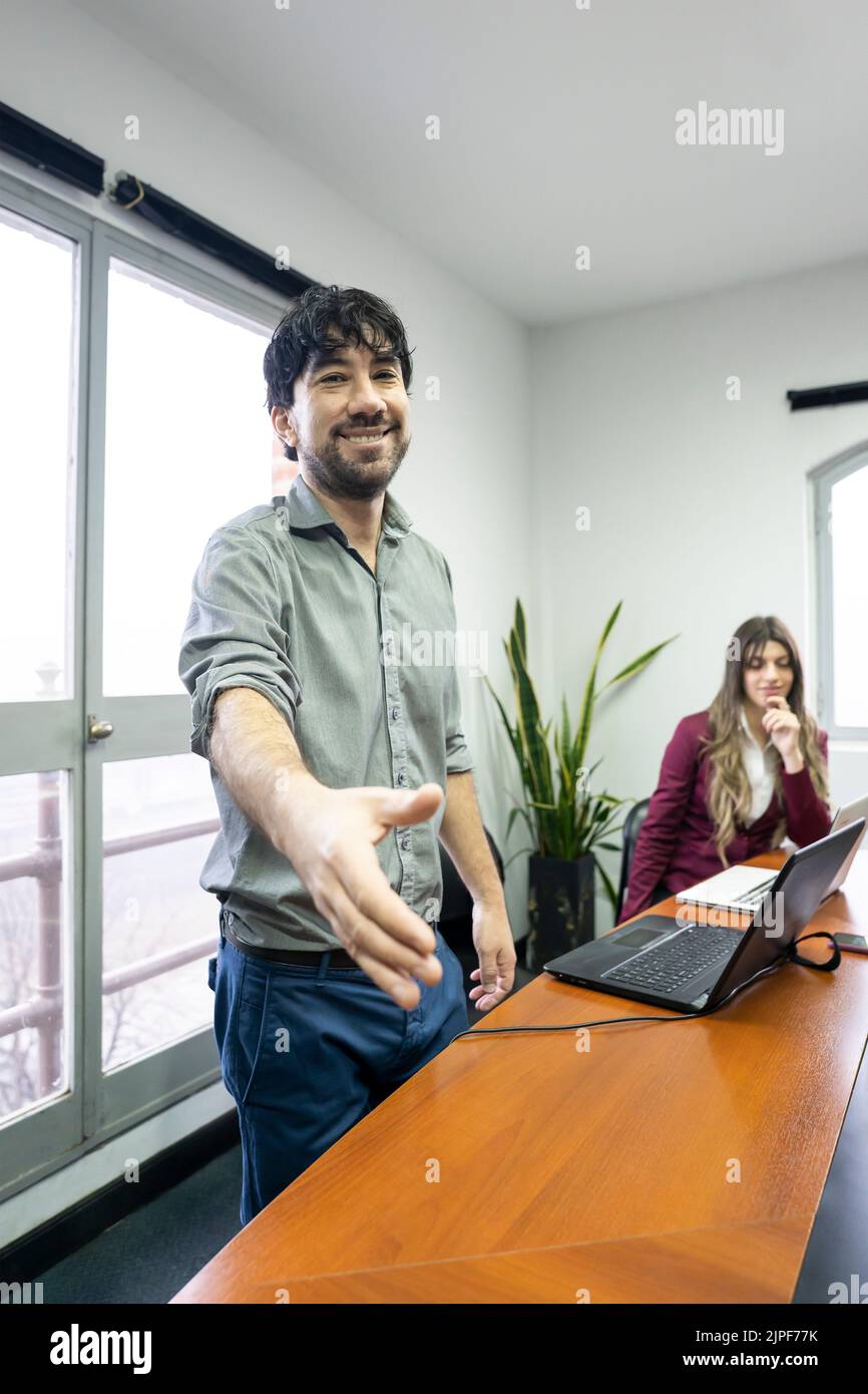 Businessman in office meeting room stands up and extends hand to greet someone out of frame. Concept of welcome, done deal, business Stock Photo