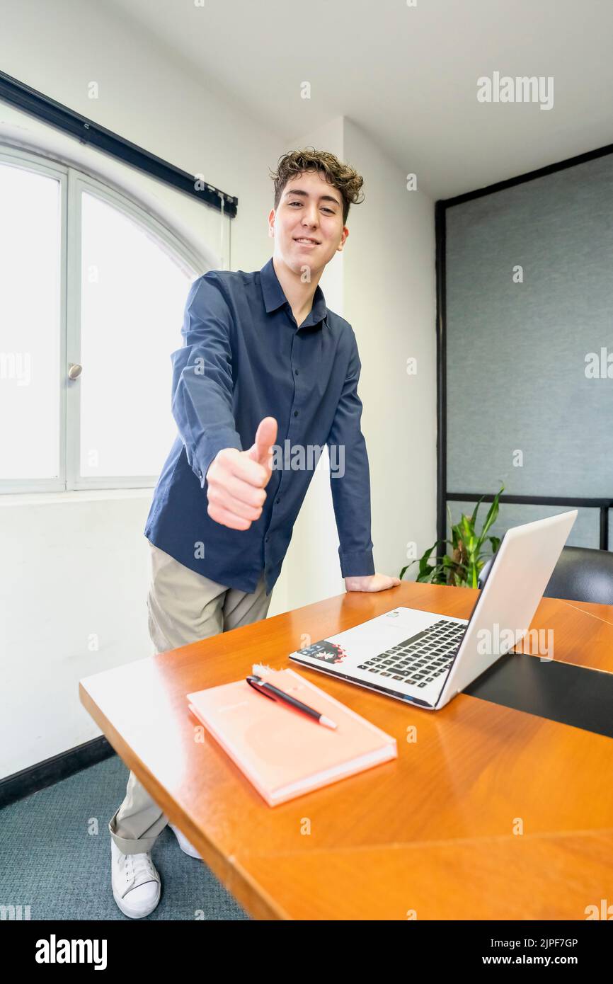 Young businessman standing at the head of the meeting table, smiling and looking at the camera with his thumb up Stock Photo