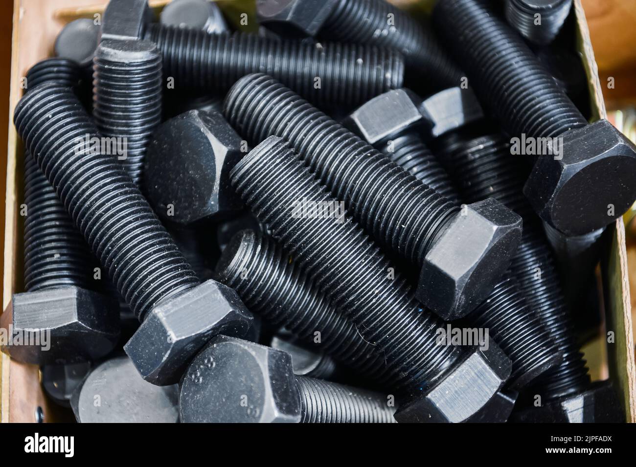 Pile of hardened blued metal bolts for fastening in crate Stock Photo