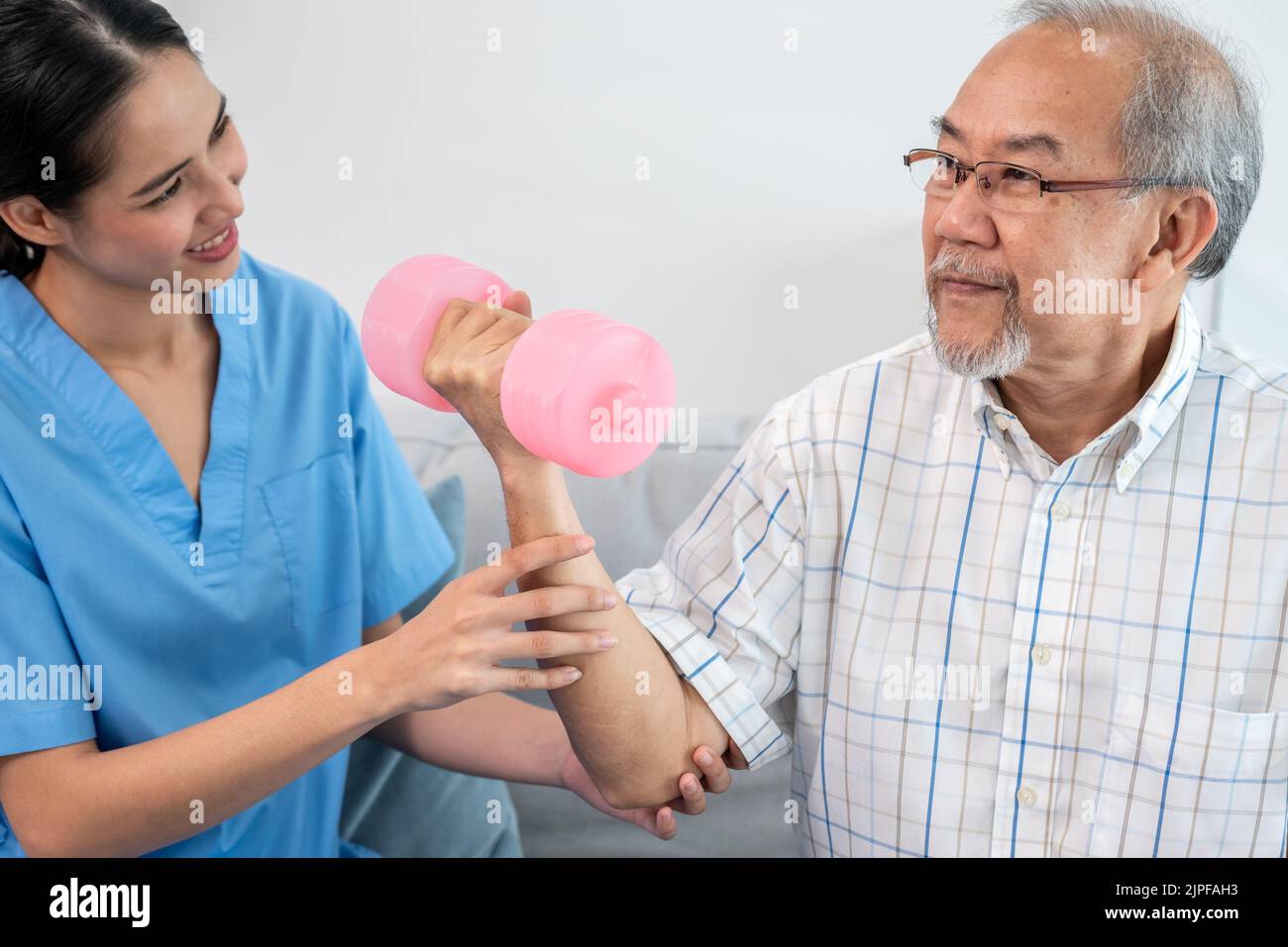 Contented senior patient doing physical therapy with the help of his caregiver. Senior physical therapy, physiotherapy treatment, nursing home for the Stock Photo