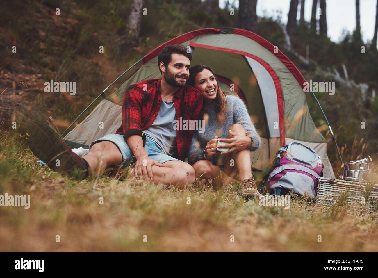 Happy young couple enjoying themselves at a campsite. Romantic young couple sitting outside a camping tent in the forest. Stock Photo