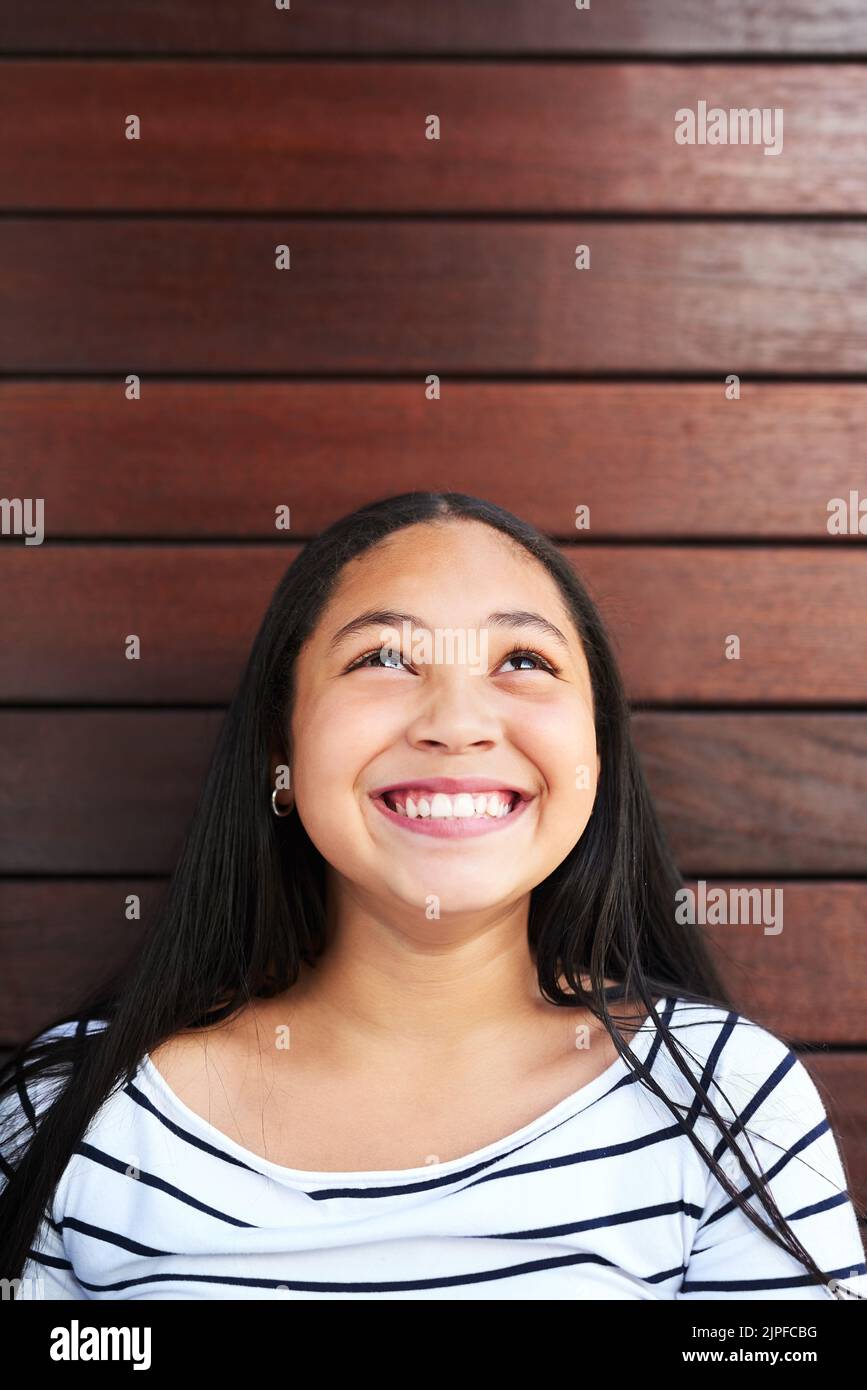 She already knows the secret to life. Keep looking up. a happy young girl posing against a wooden background and looking up. Stock Photo