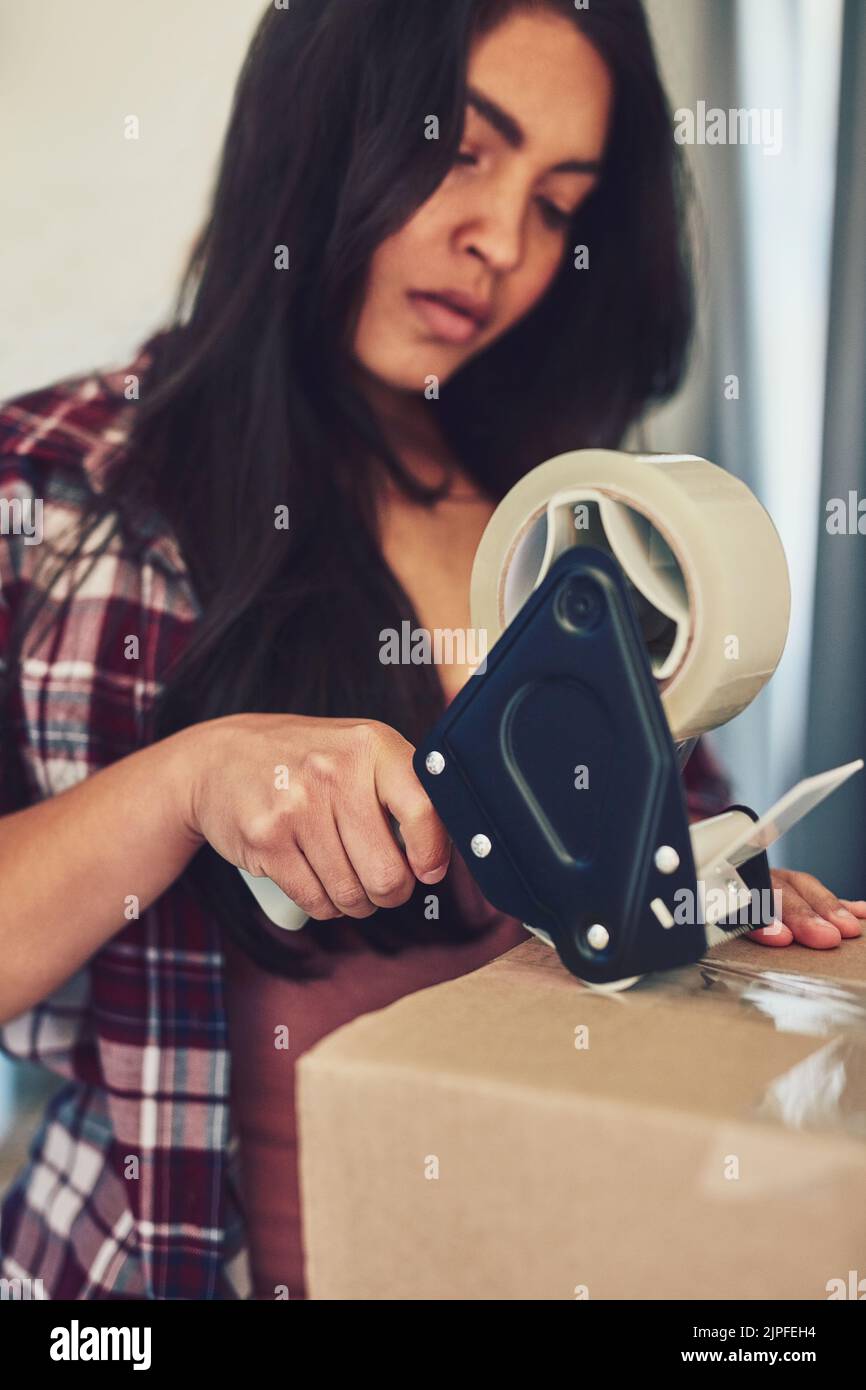 Moving day is finally here. a young woman using tape to pack boxes