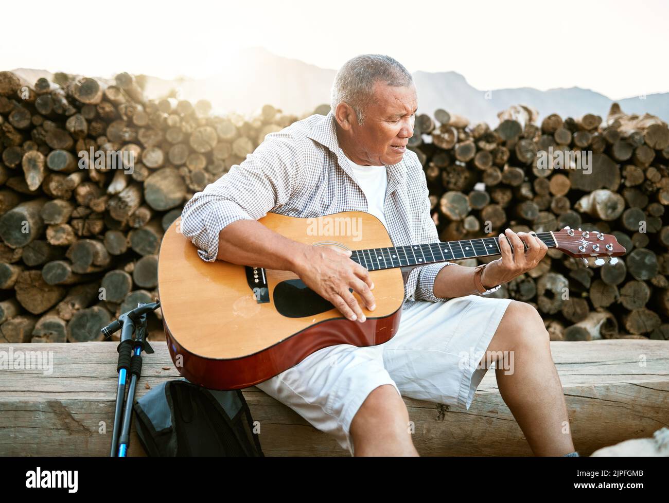 . Mature man, relaxing and playing the guitar while sitting outdoors and enjoying his hobby while getting fresh air. Older man singing a song in his Stock Photo