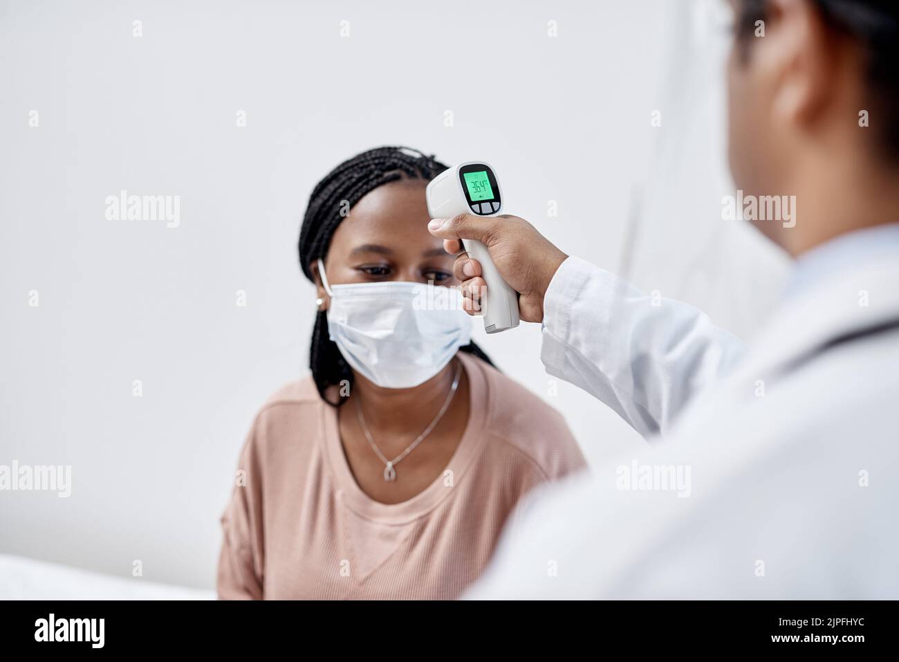 Doctor taking temperature of a covid patient while testing for high fever symptoms of sick, flu or illness. Screening woman for a healthcare consult Stock Photo