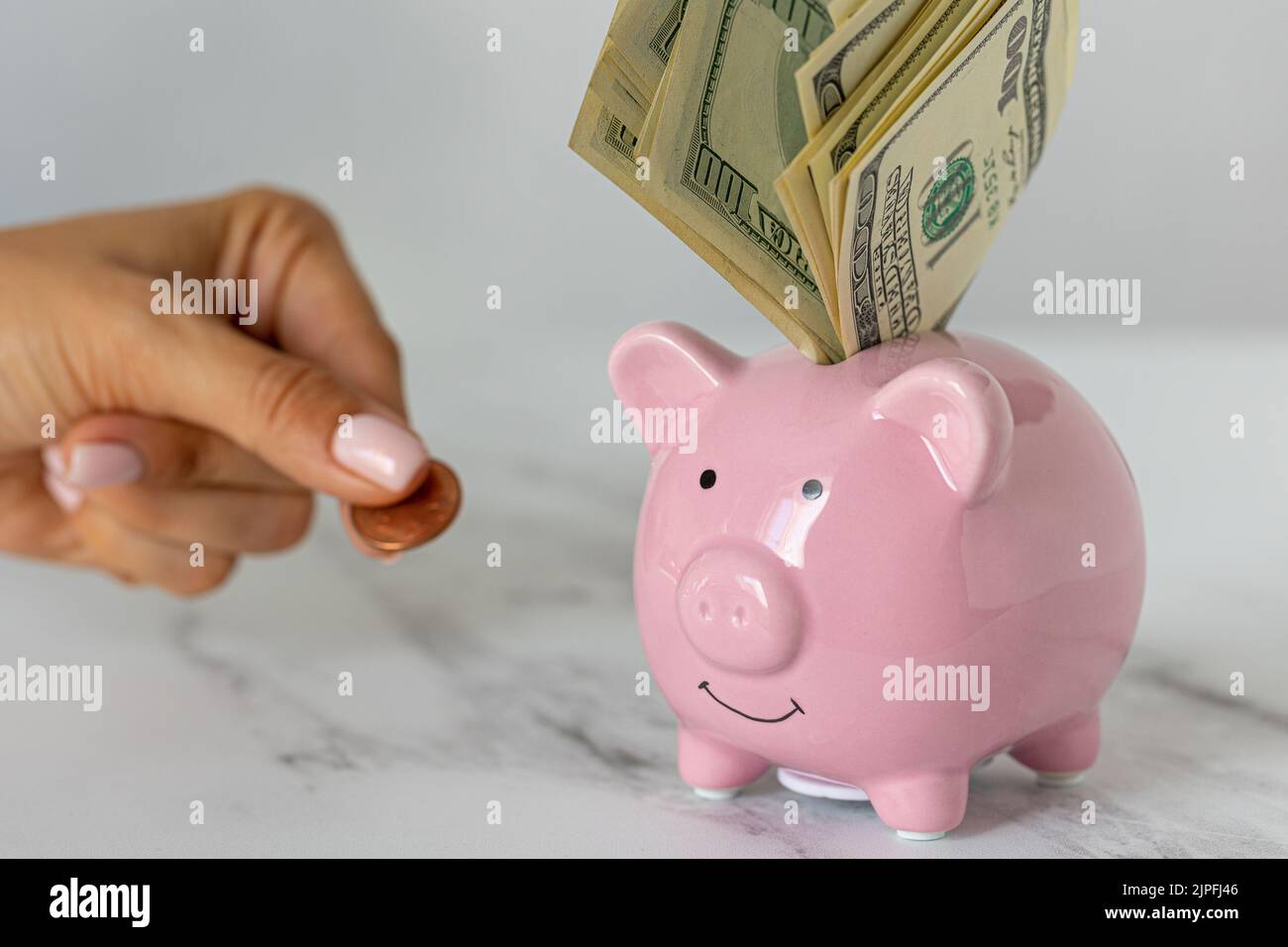 Close-up of a piggy bank with dollars and a woman's hand holding out euro coins on the office table. economy, crisis and inflation. Cost Management Stock Photo