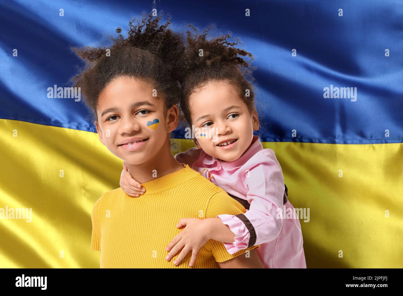 Cute African-American sisters against national flaf of Ukraine Stock Photo