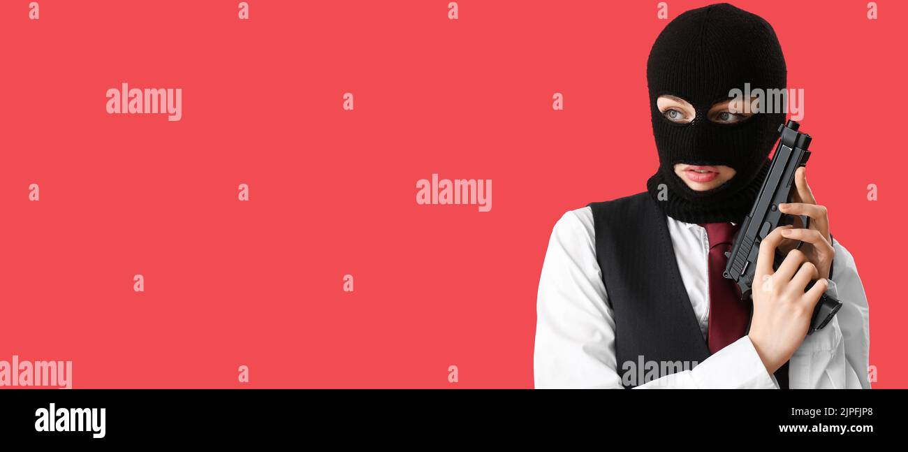 Portrait of young woman in balaclava and with gun on red background with space for text Stock Photo