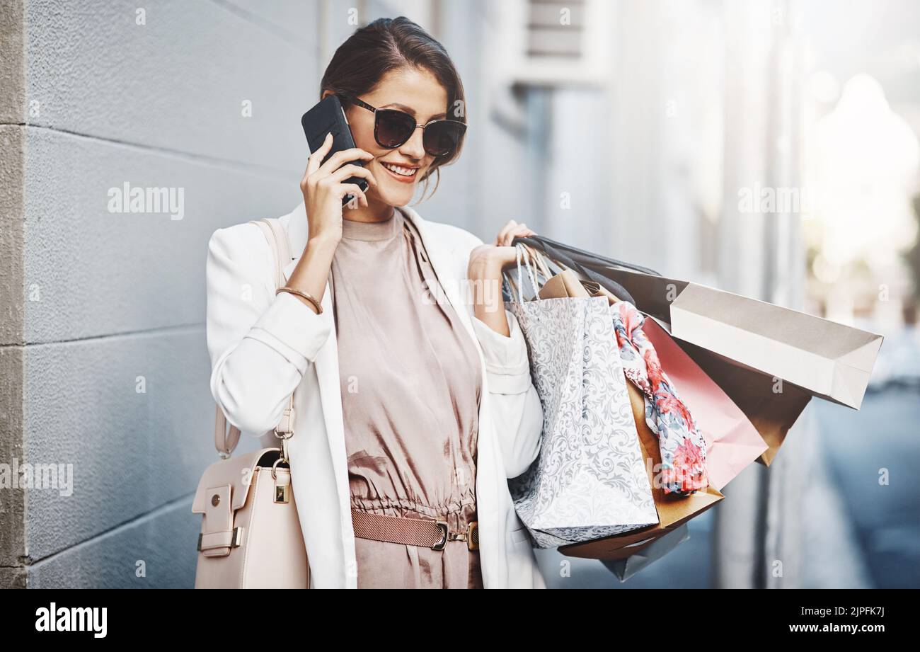 Trendy, stylish and fashionable woman shopping, purchasing and buying clothes in city, town and downtown. Elegant lady talking on phone with gift bags Stock Photo