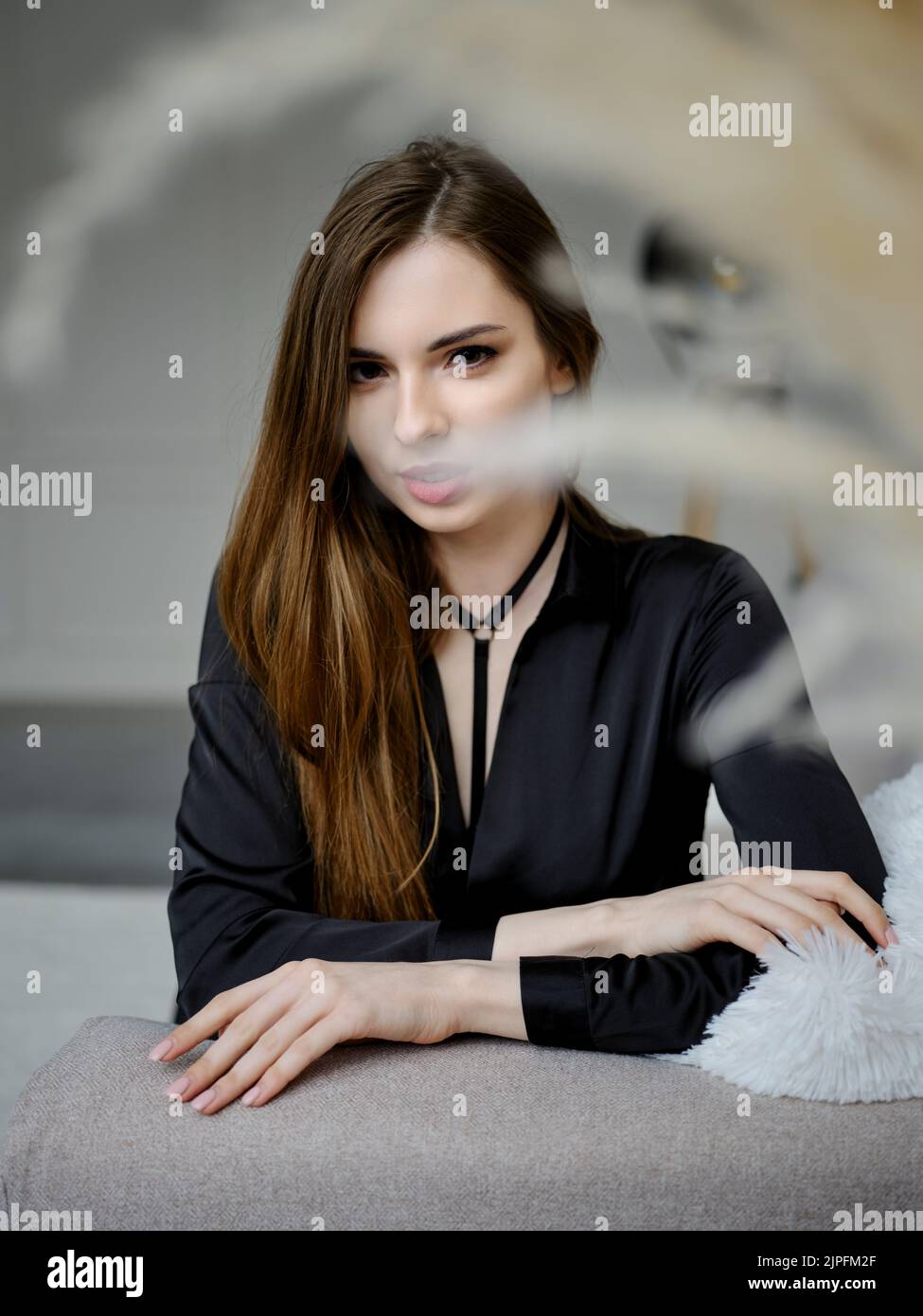 Cute young woman sitting on sofa and looking straight to the camera ...