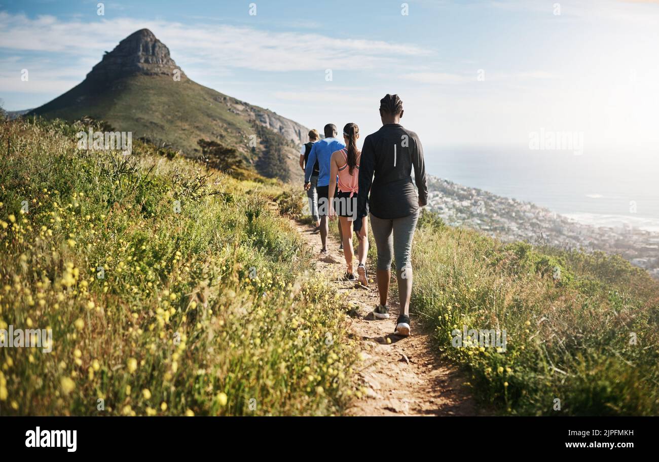 It benefits you in more ways than one. Rearview shot of a group of people walking on a path through the mountains. Stock Photo