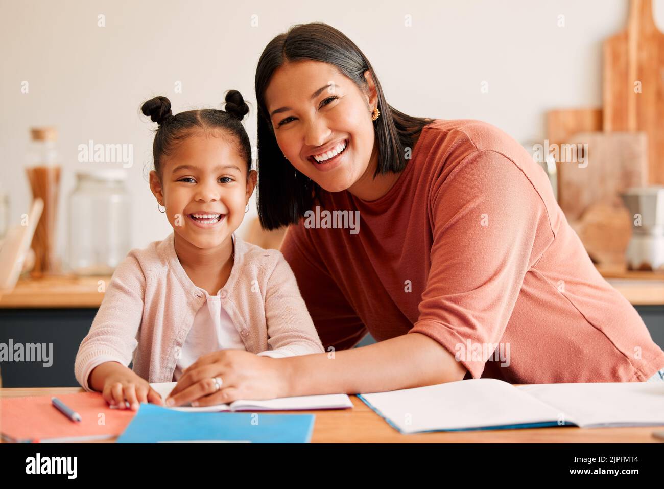 Mother helping, teaching and educating daughter with homework at home. Portrait of happy, loving and smiling mom and little girl busy with educational Stock Photo