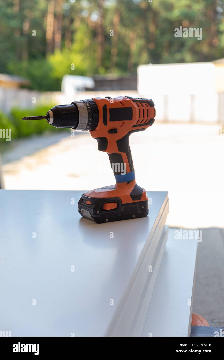 Cordless screwdriver stands on a wooden panel. A wireless tool for working outdoors in the absence of an electrical network. Stock Photo