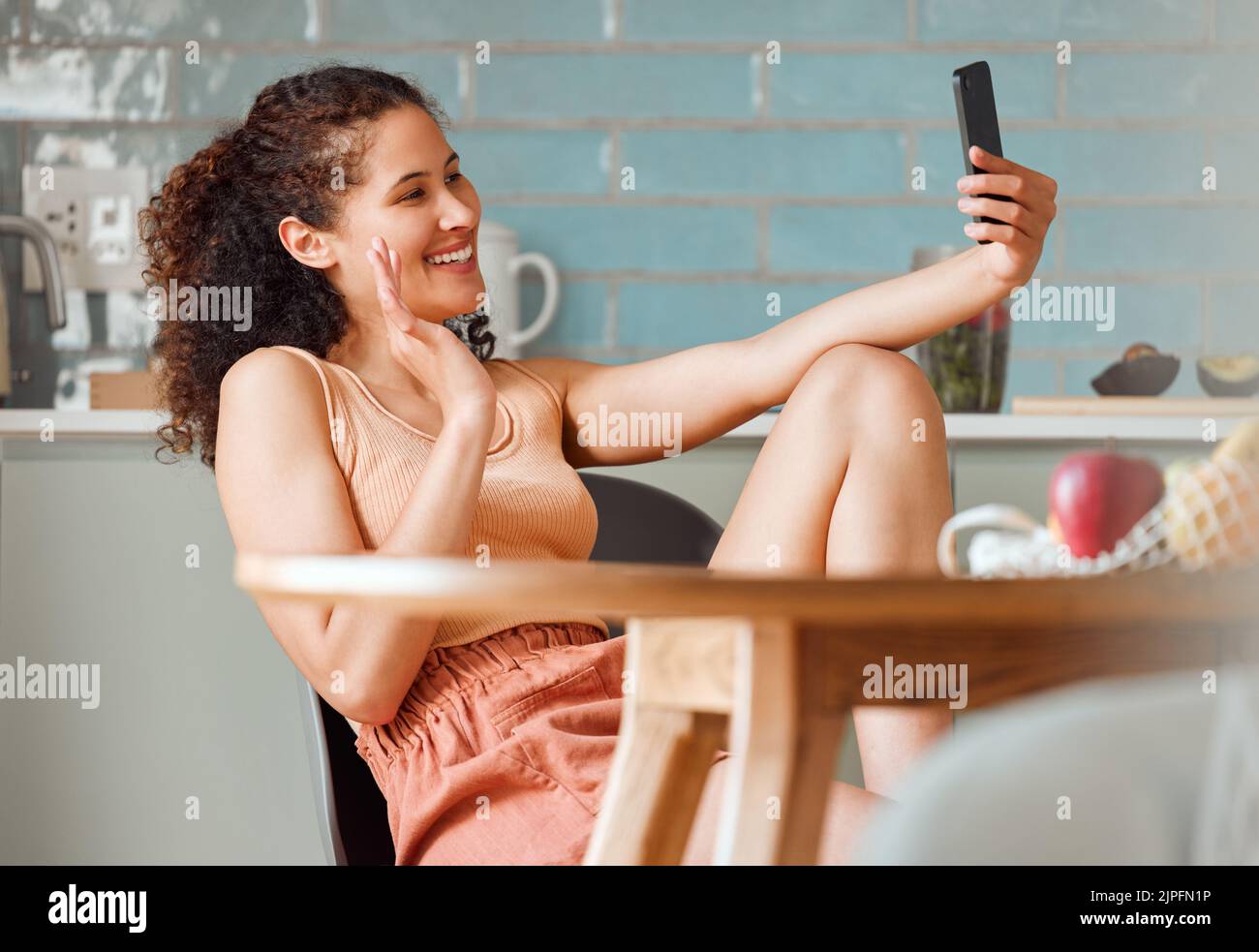 Woman waving on video call with phone, greeting and talking in online chat with webcam at home. Smiling, happy and relaxed female having conversation Stock Photo