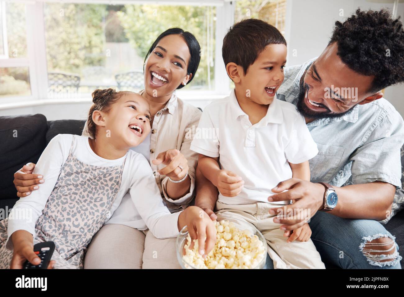 Family watching tv or a movie, having fun and eating popcorn together at home. Love and laughter with affectionate parents and happy children smiling Stock Photo