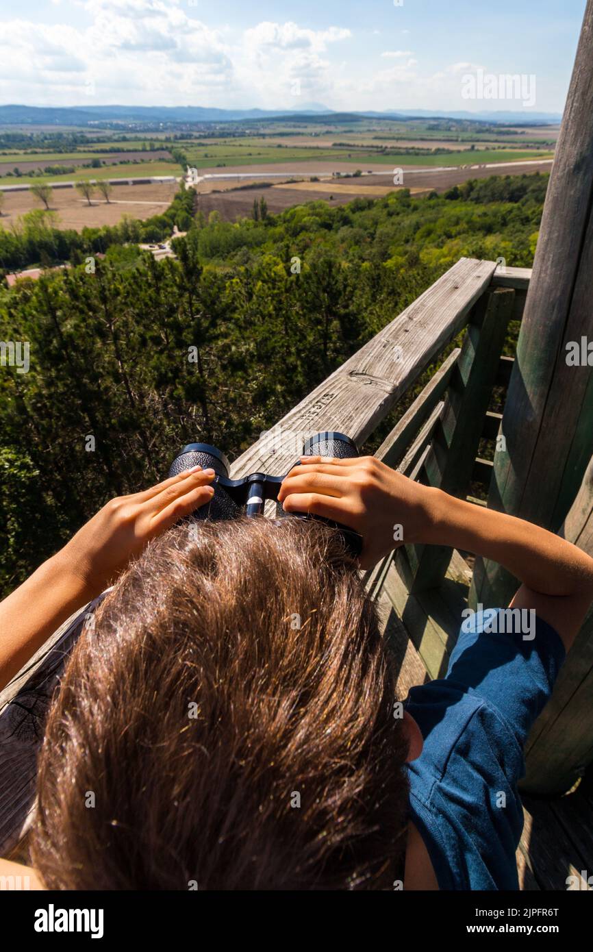 Boy child looking through binoculars on top of Hubertus lookout tower towards south-west, Sopron, Hungary Stock Photo