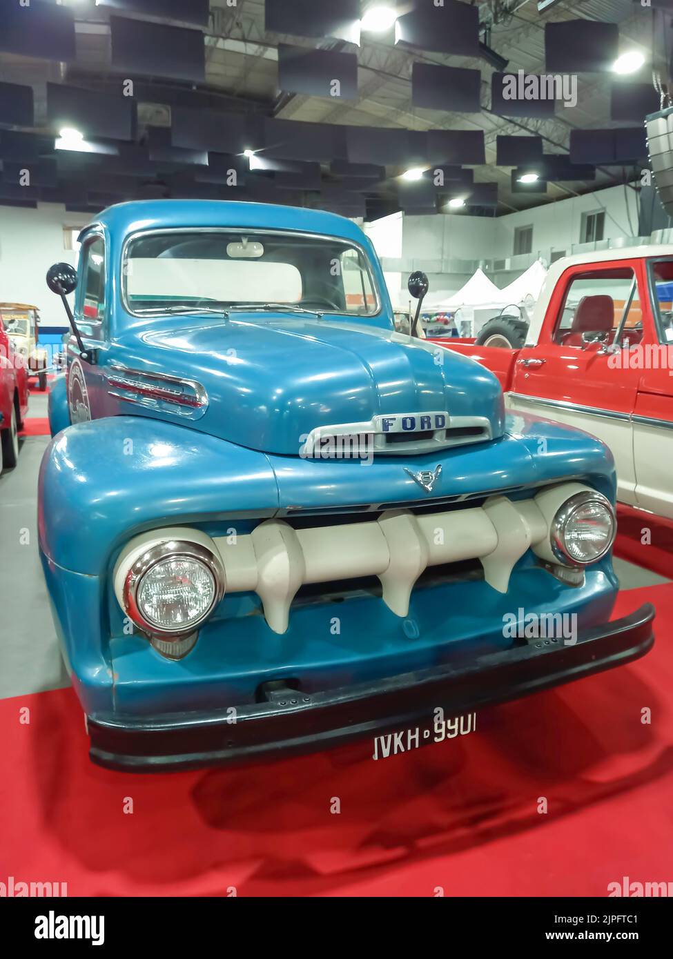 Old blue 1951 Ford F 1 V8 utility pickup truck on a red carpet. Front view. Grille. Exhibit hall. Classic car show. Stock Photo