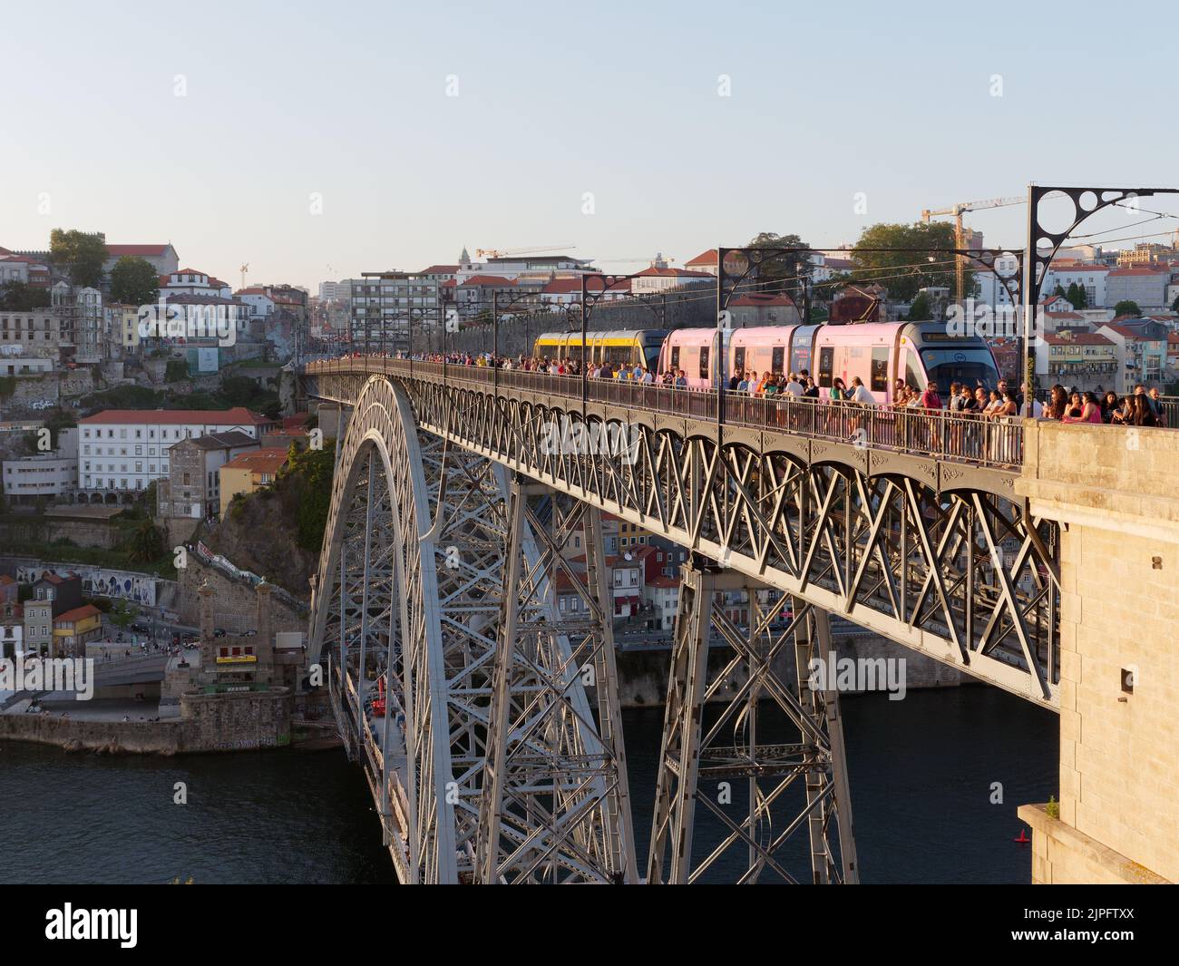 Ribeira district in Porto town across the Douro River as people admire the view from Luis I bridge and a metro train crosses the bridge, Portugal. Stock Photo