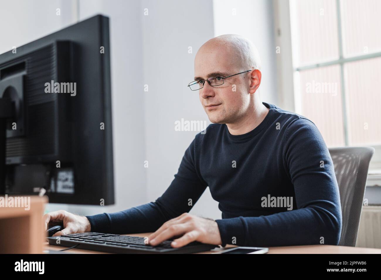 Young Entrepreneur Wearing Eyeglasses Sitting at his Table Inside the Office, Looking at the Report on his Computer Screen. Stock Photo