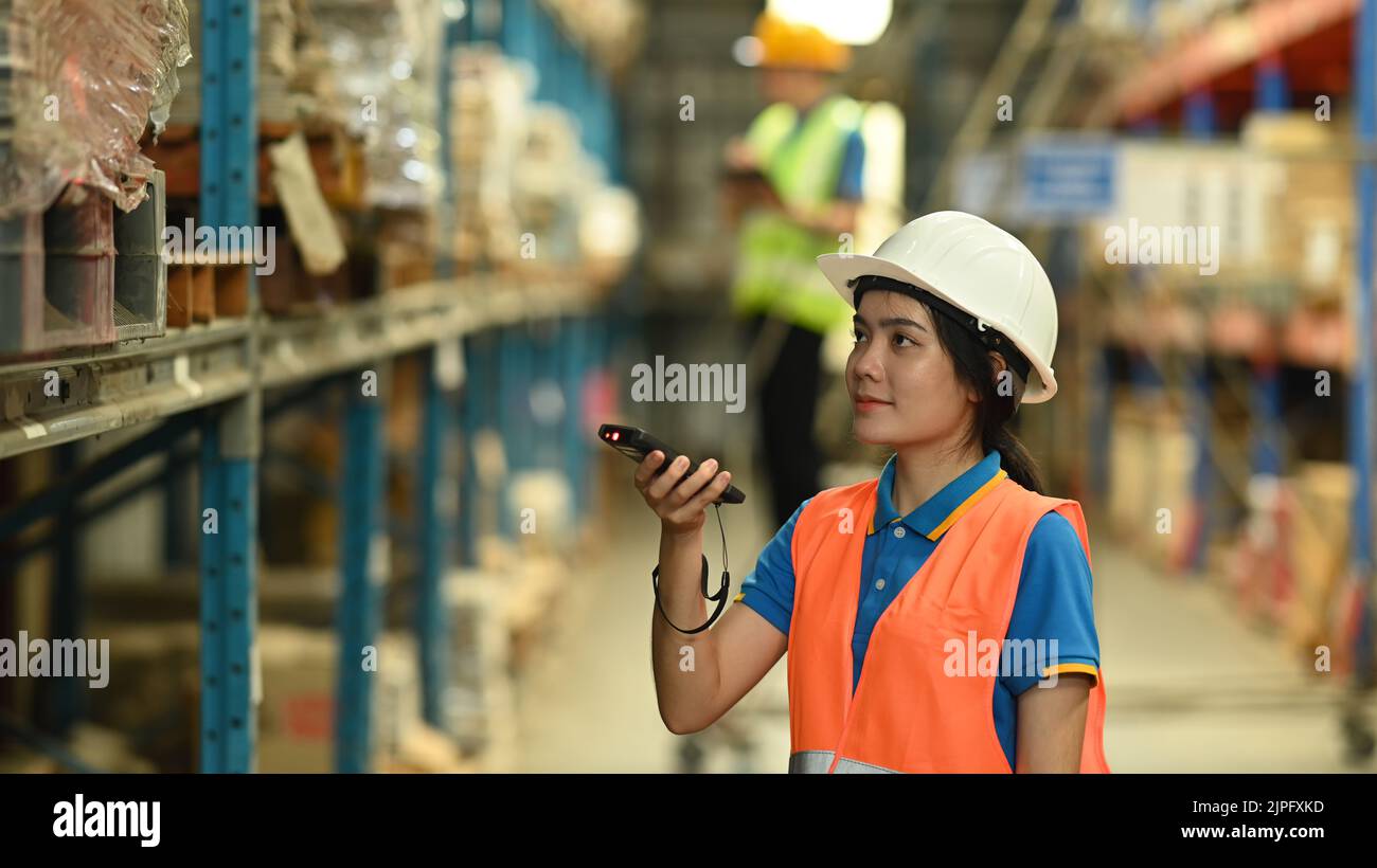Female warehouse worker wearing safety hard hat and vest scanning
